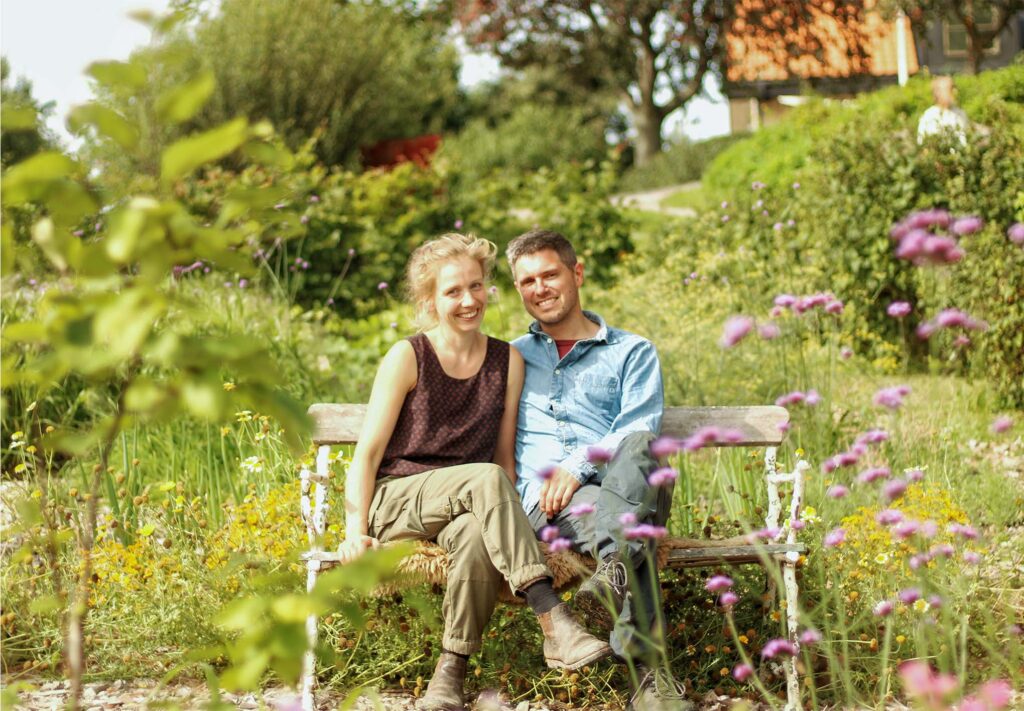 Franziska och Niko sitter på en bänk i den lummiga trädgården på Kulturodling